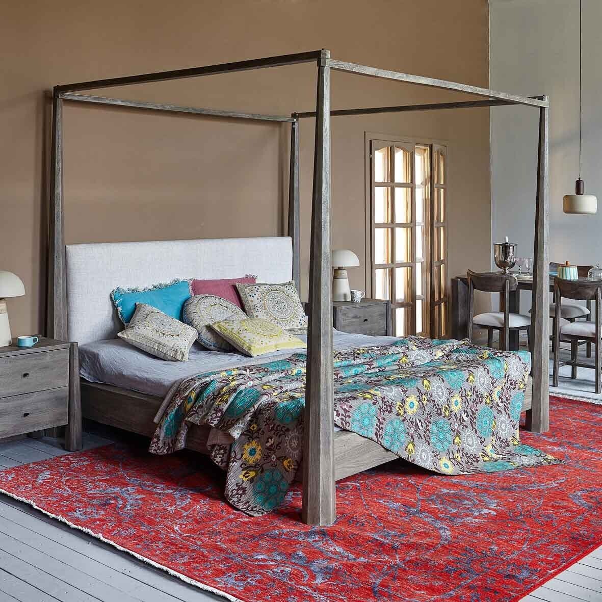 Bedroom with a canopy bed featuring colorful bedding and pillows on a red patterned rug.