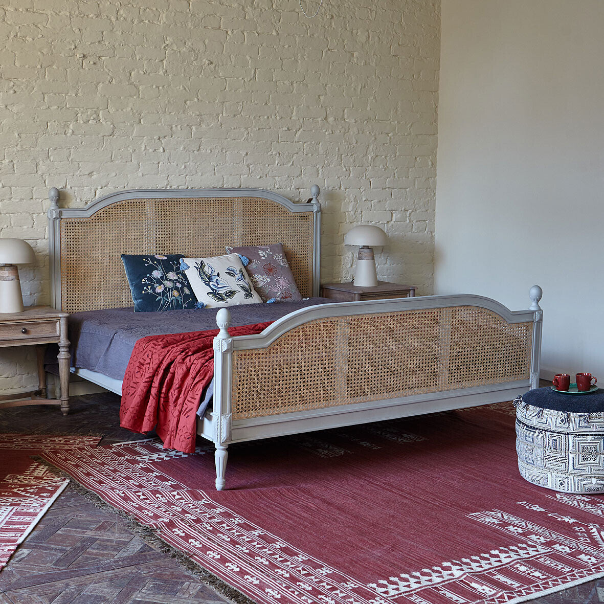 Bedroom with a bed featuring a wicker headboard and footboard, red blanket, and patterned pillows.