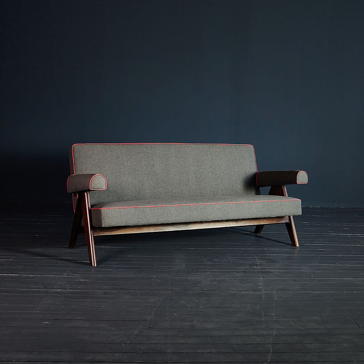 Gray sofa with wooden frame on a dark floor and wall