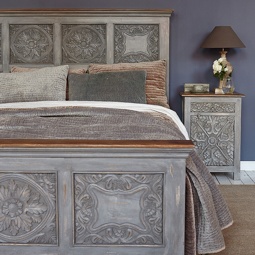 Decorative bed with intricate carvings and a matching nightstand against a purple wall.