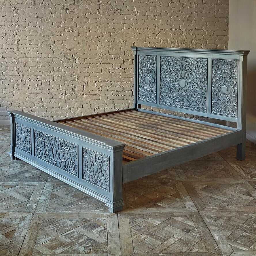 Decorative wooden bed with intricate carvings against a brick wall.
