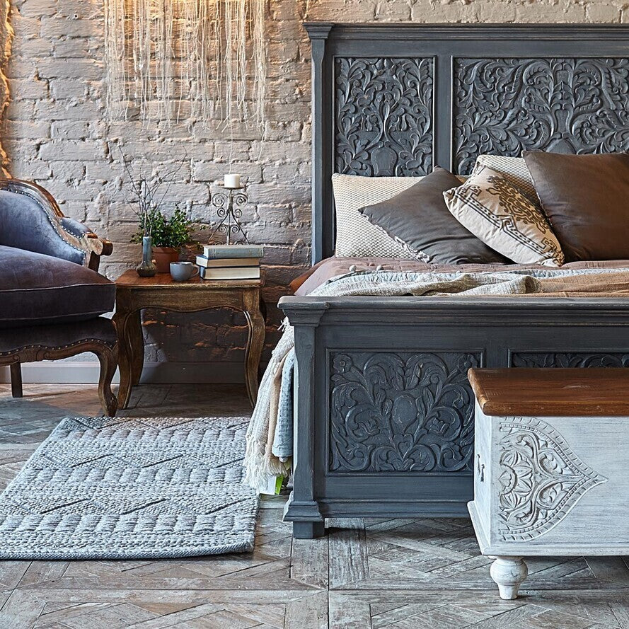Decorative bedroom with a gray upholstered bed and ornate headboard.