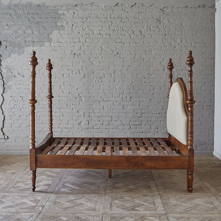 Wooden bed with a white headboard against a gray brick wall.