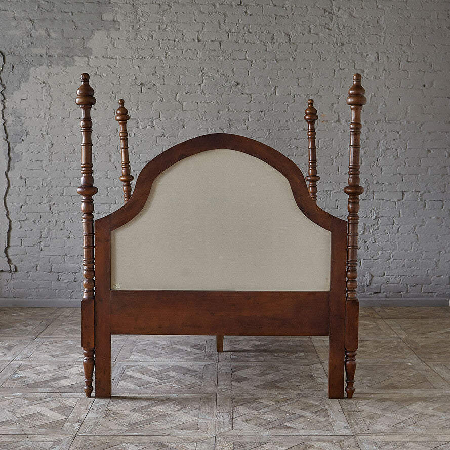 Wooden bed frame with a beige upholstered headboard against a brick wall.