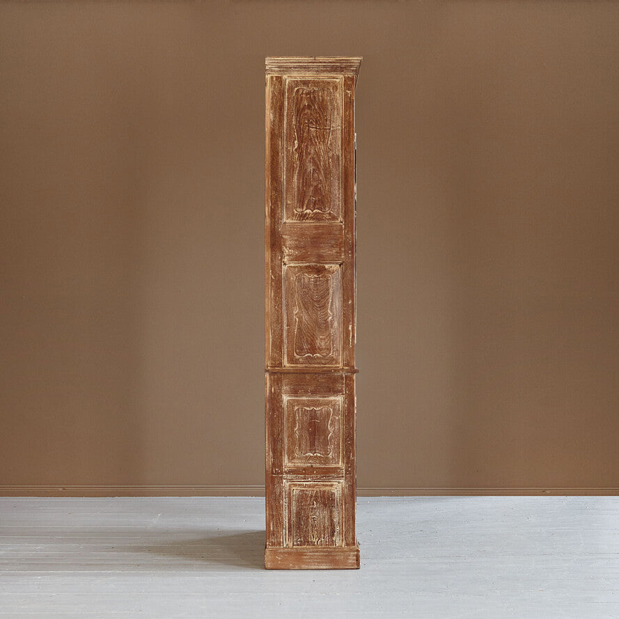 Tall wooden cabinet with carved panels against a brown wall
