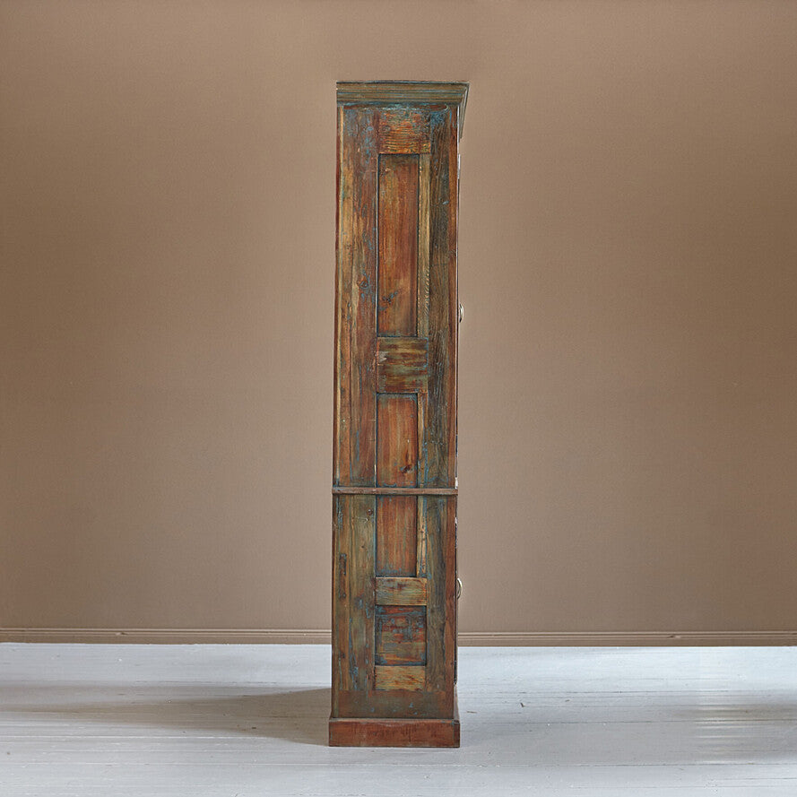 Tall, narrow wooden cabinet with a distressed finish against a plain wall.
