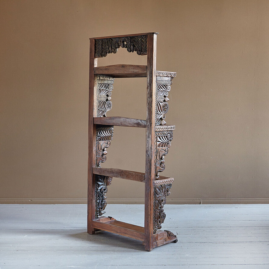 Wooden bookshelf with intricate carvings against a beige wall.