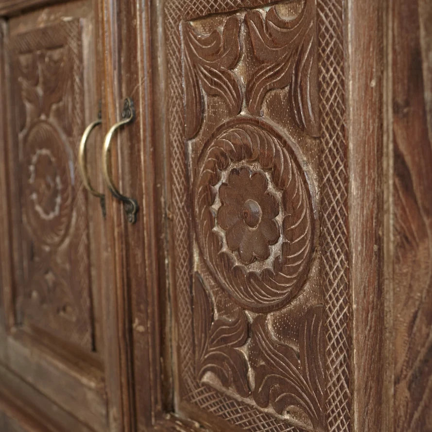 Close-up of a wooden cabinet with intricate carvings and a brass handle.