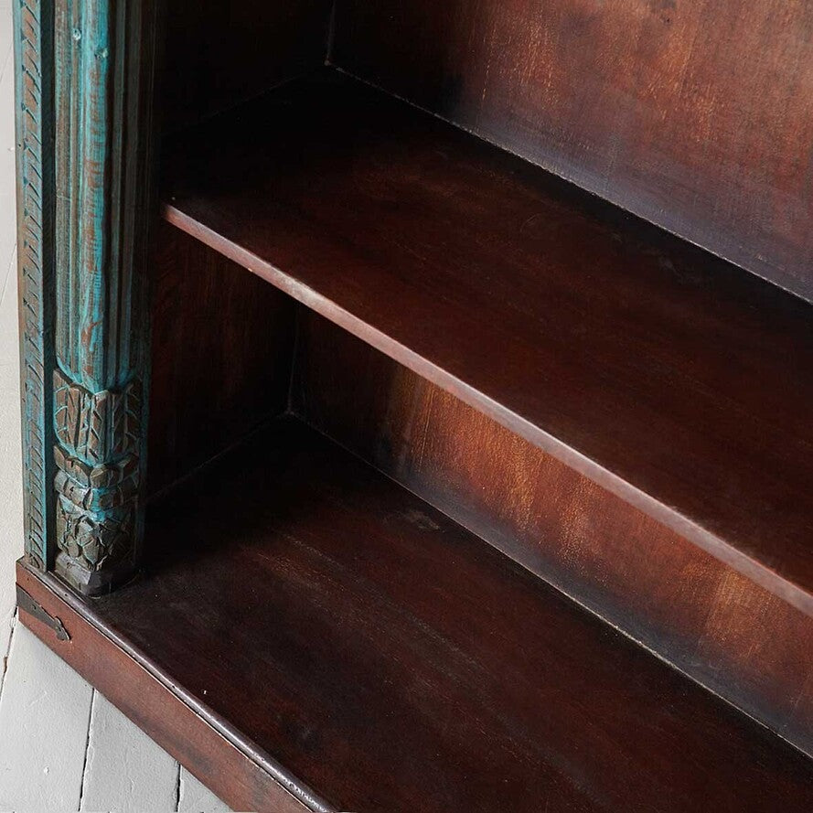 Close-up of a wooden shelf with decorative carvings on a white wall.