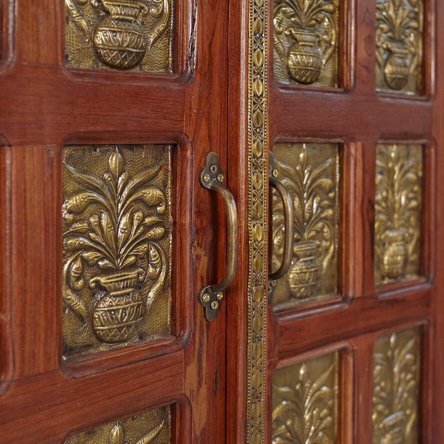 Close-up of a wooden door with brass decorative panels and a handle.