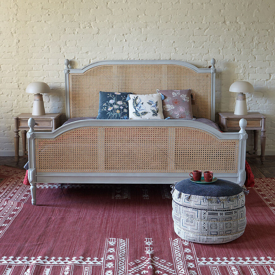 Wicker bed with decorative pillows in a room with a brick wall and patterned rug.