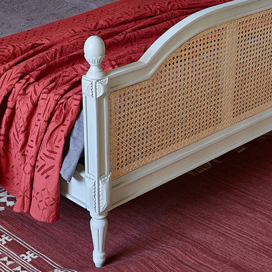 Bed with wicker headboard and red bedding on a red carpet