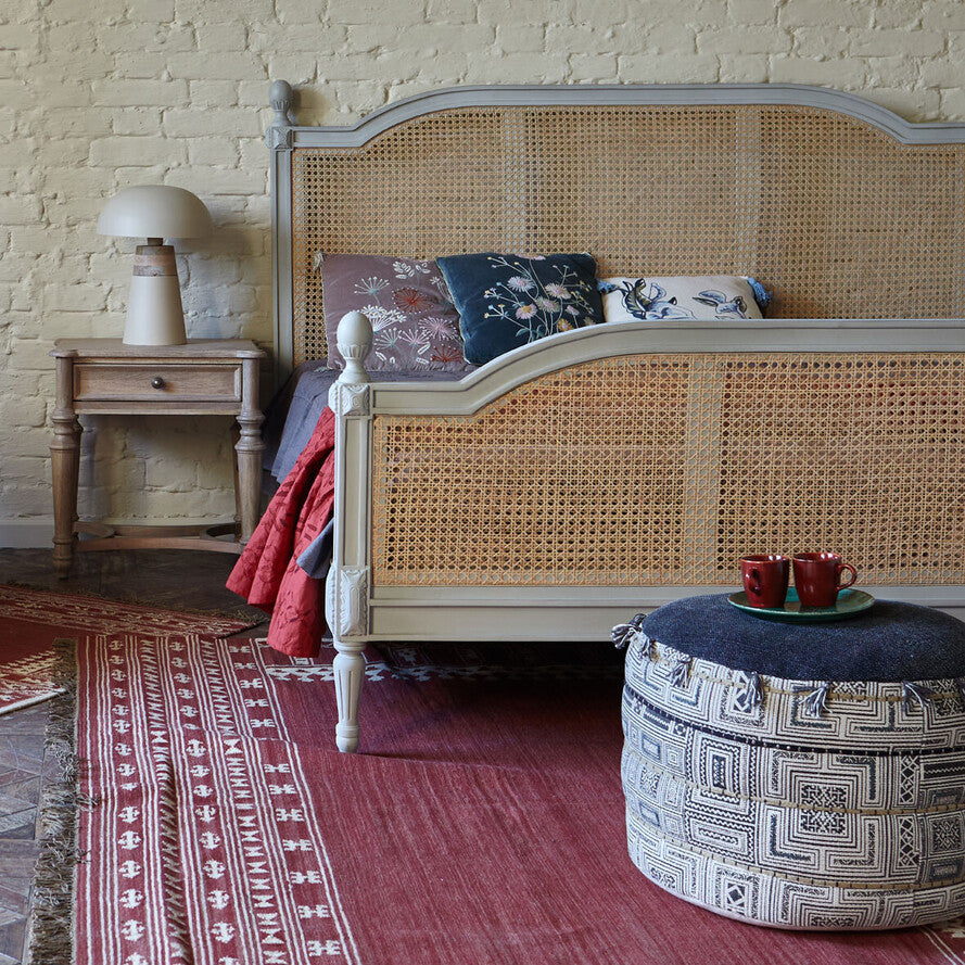 Bedroom with wicker bed, patterned rug, and ottoman with cups.