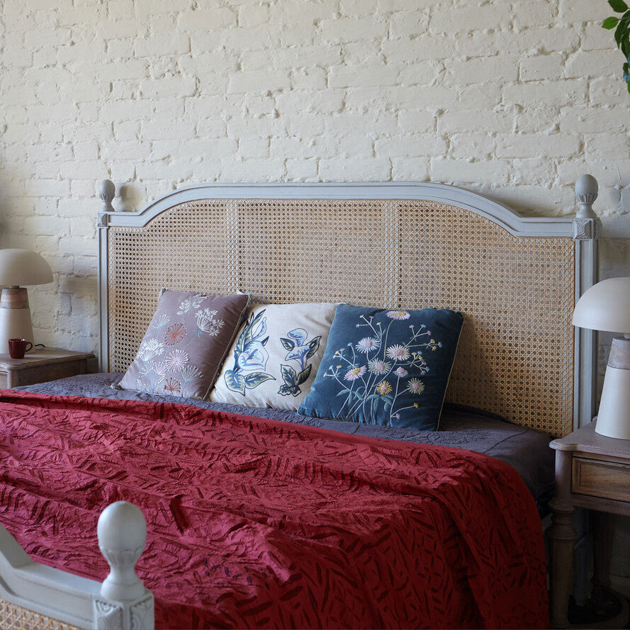 Bed with wicker headboard and red blanket against a white brick wall