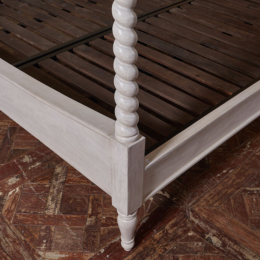 Wooden bed frame with white spindle posts on a wooden floor.