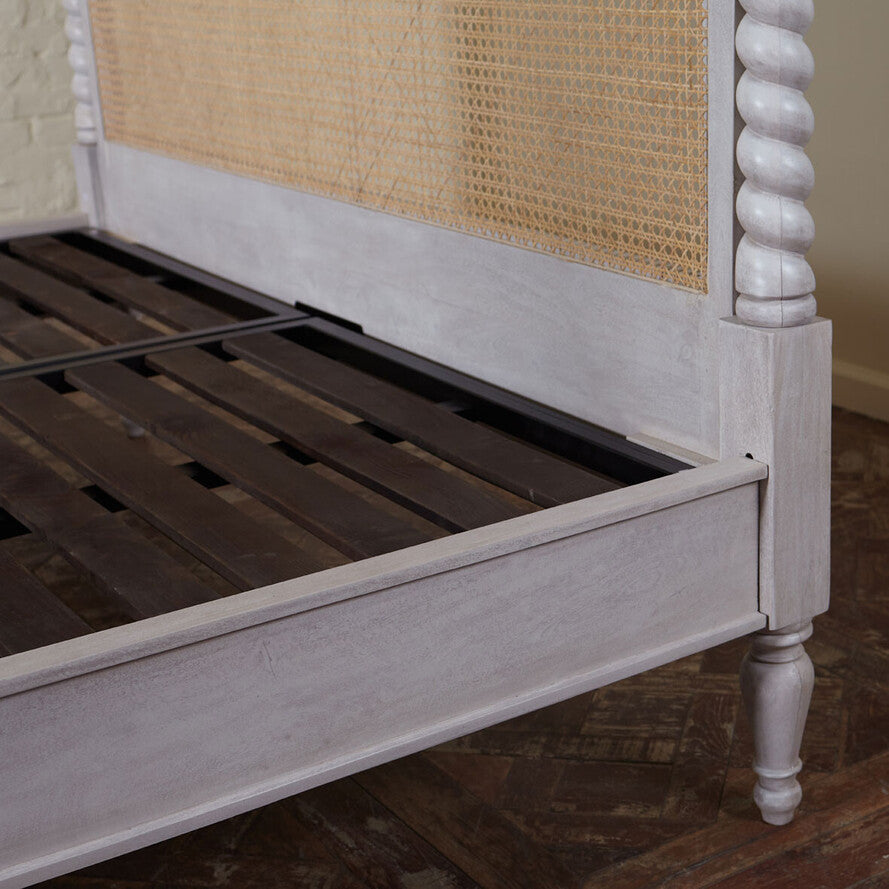 Wooden bed frame with wicker headboard on a wooden floor.