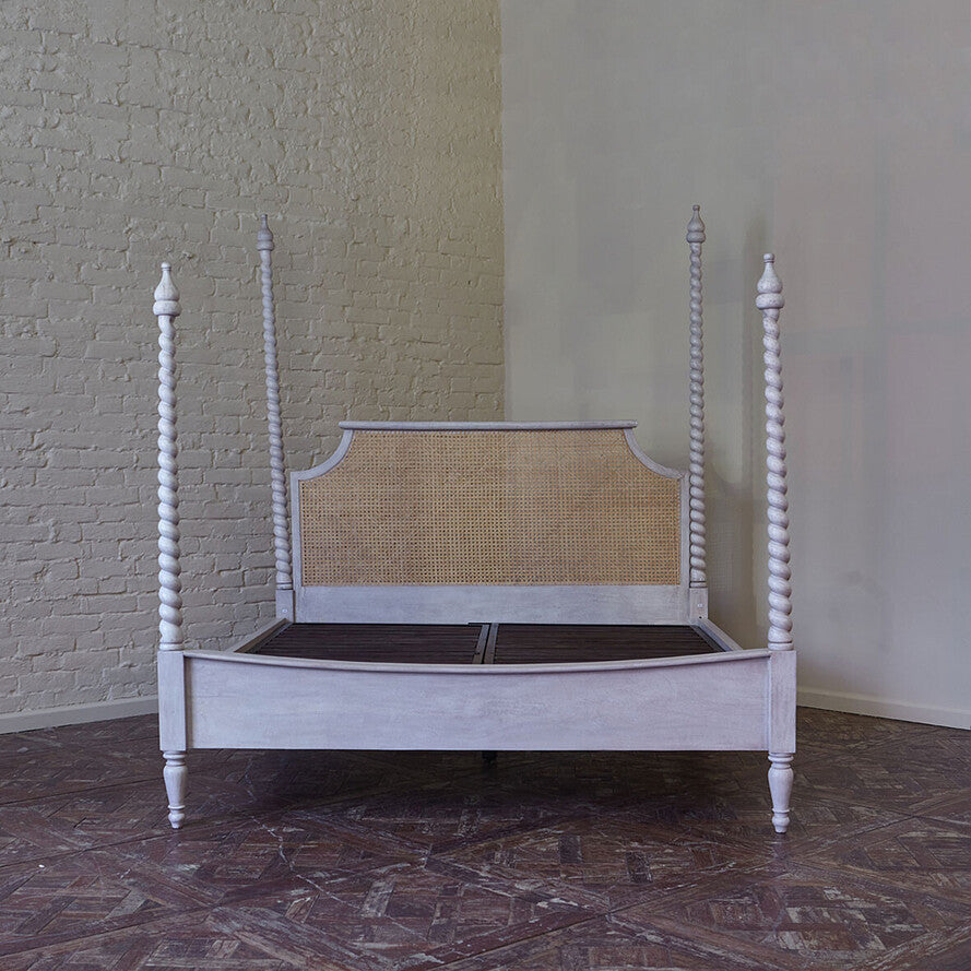 White four-poster bed with wicker headboard against a textured wall.