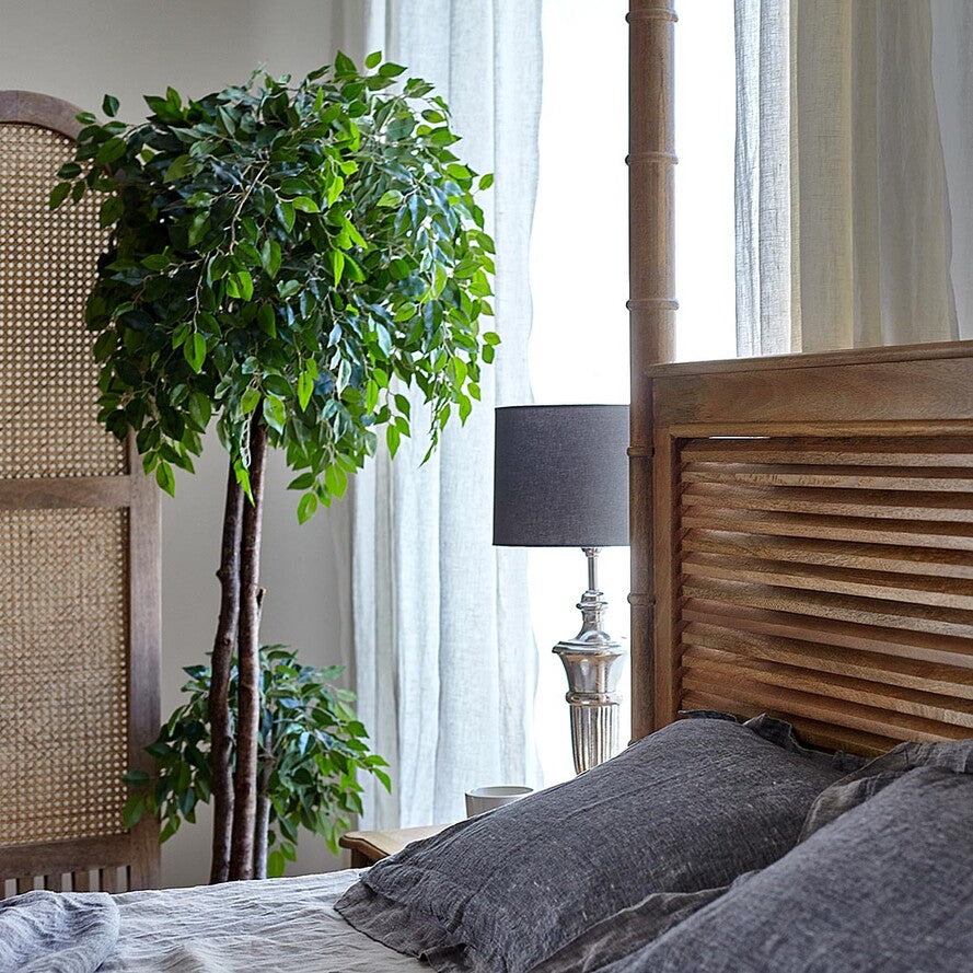 Bedroom with wooden headboard, gray pillows, and a potted plant.