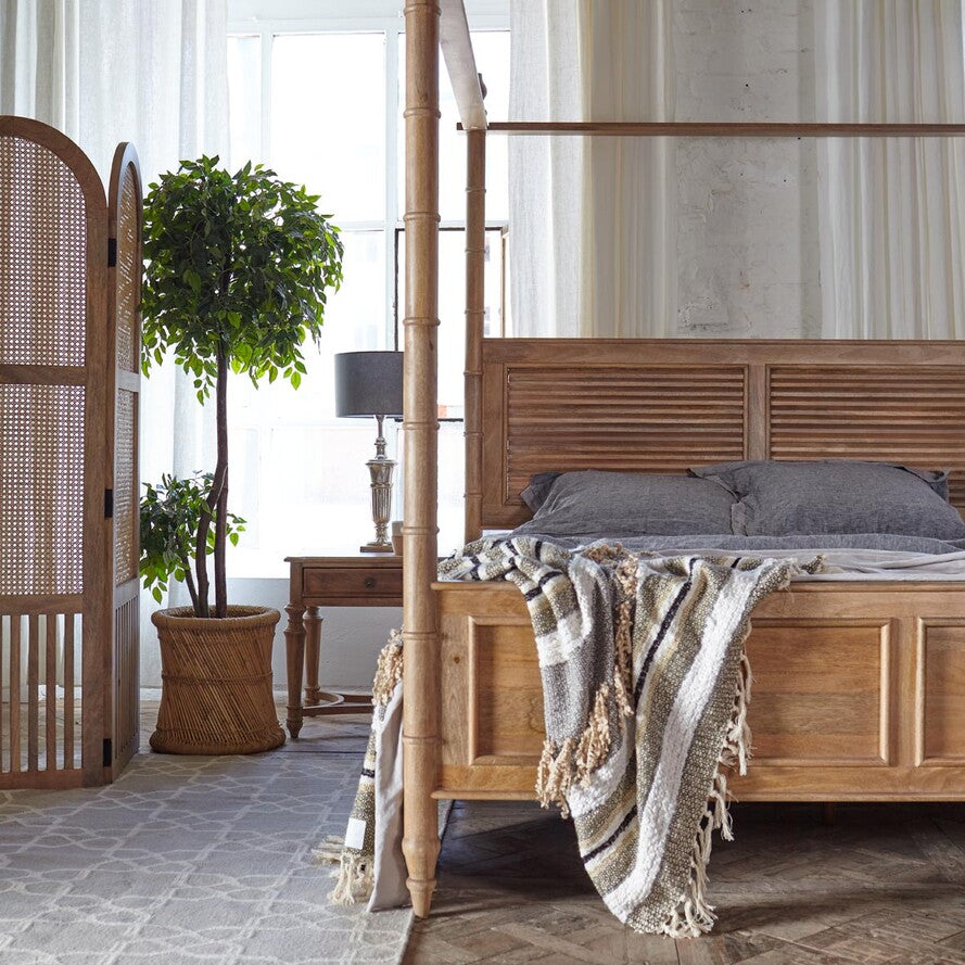Wooden four-poster bed in a bedroom with a plant and lamp.