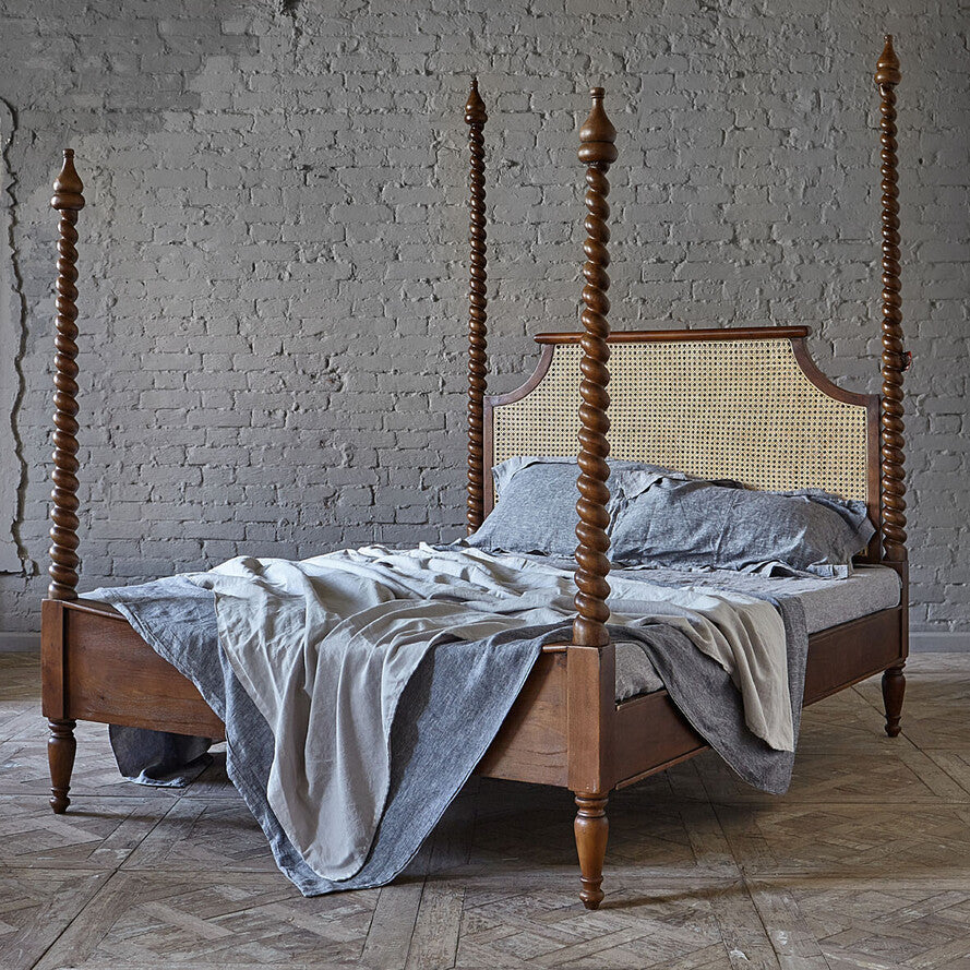 Wooden four-poster bed with gray bedding against a brick wall.