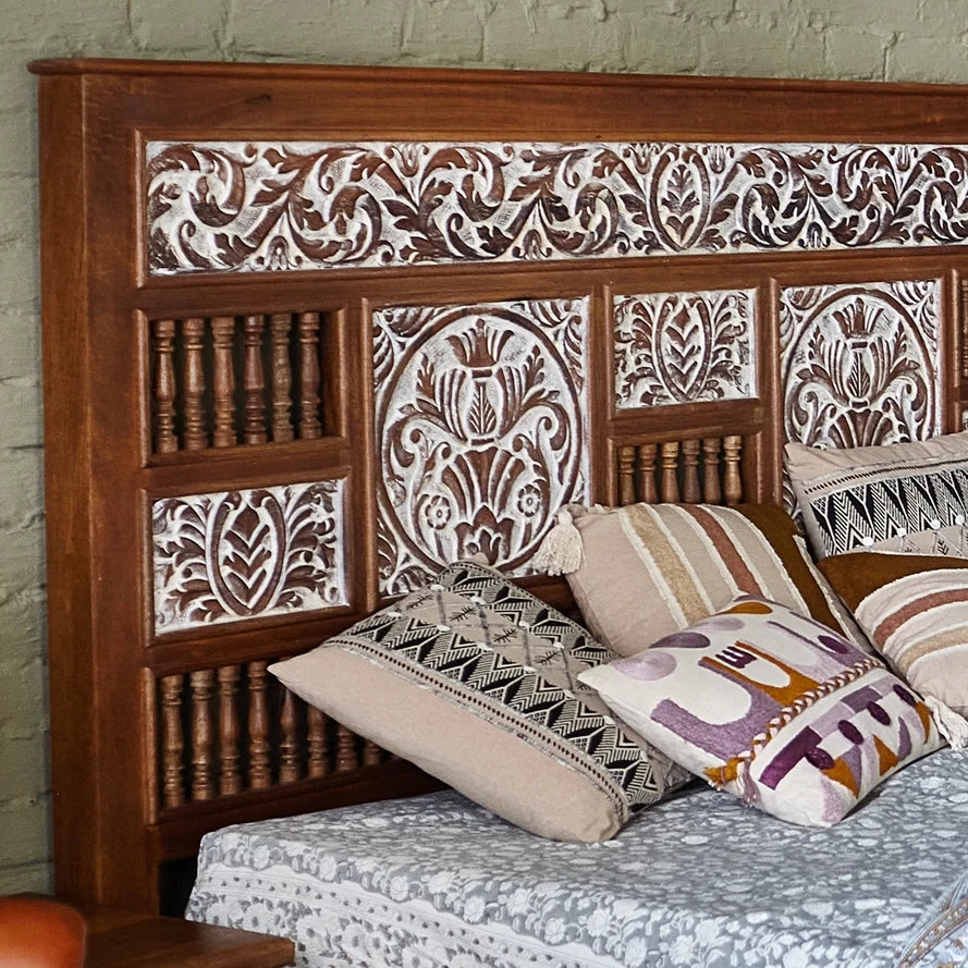 Wooden headboard with intricate carvings and patterned pillows on a bed.