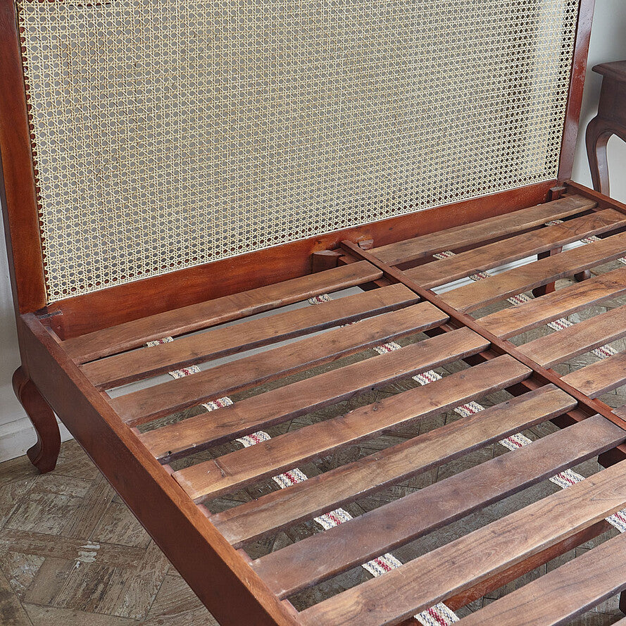 Wooden bed frame with woven headboard on a wooden floor.