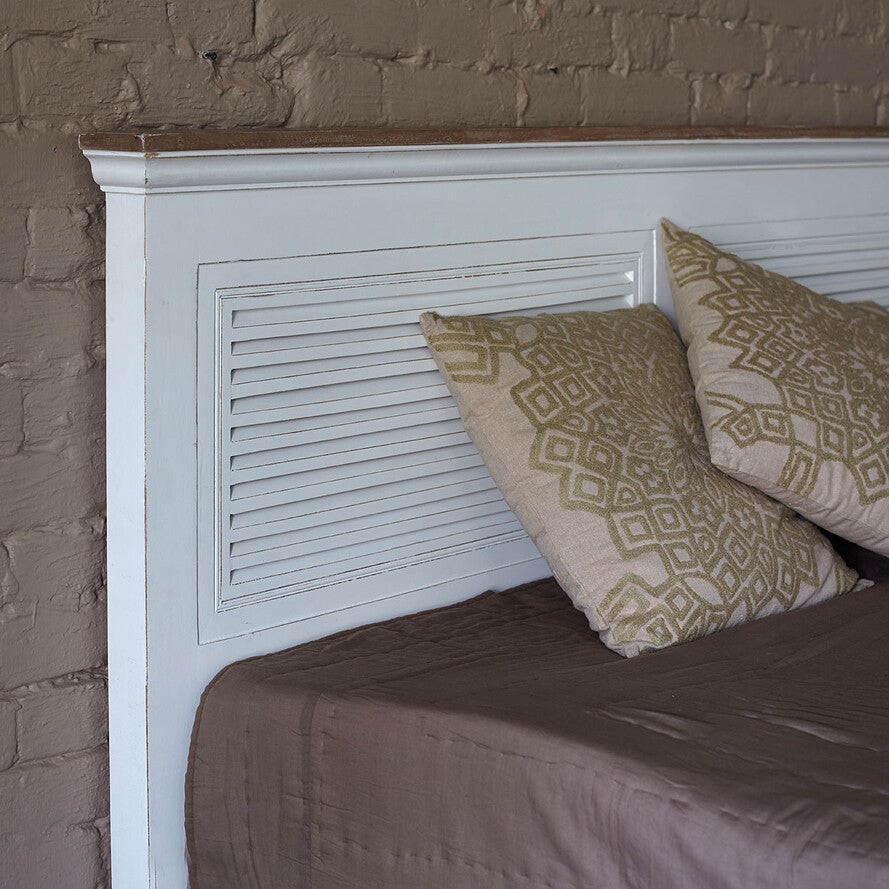 Bed with white headboard and patterned pillows against a brick wall.