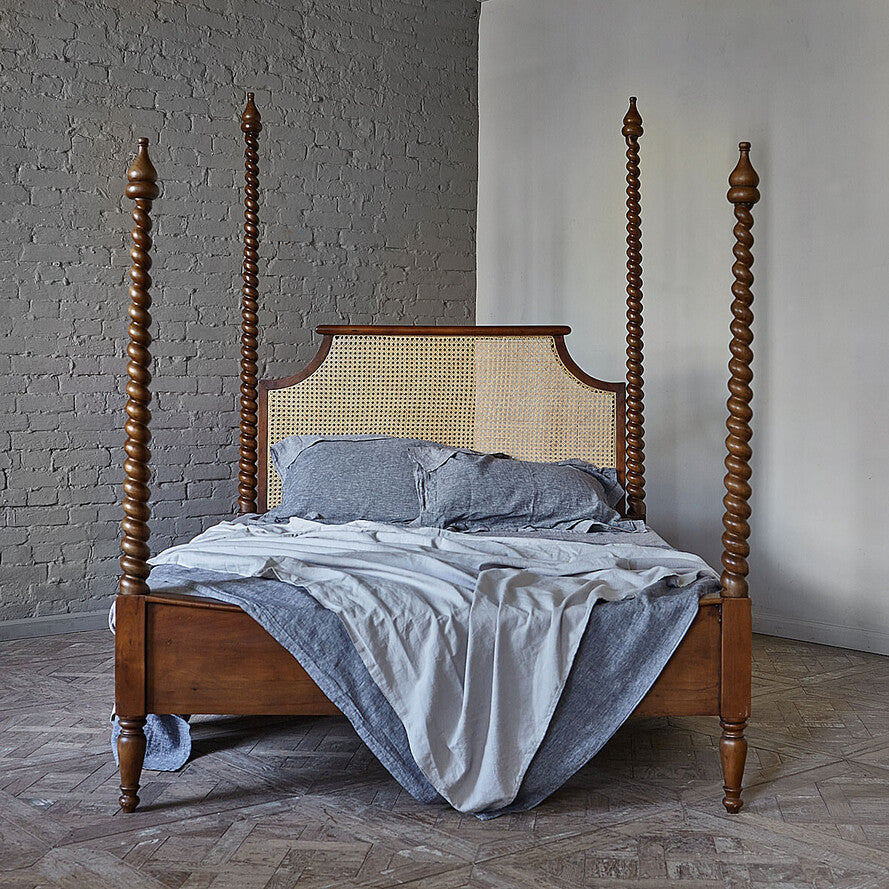 Wooden four-poster bed with a wicker headboard in a room with gray walls and wooden flooring.