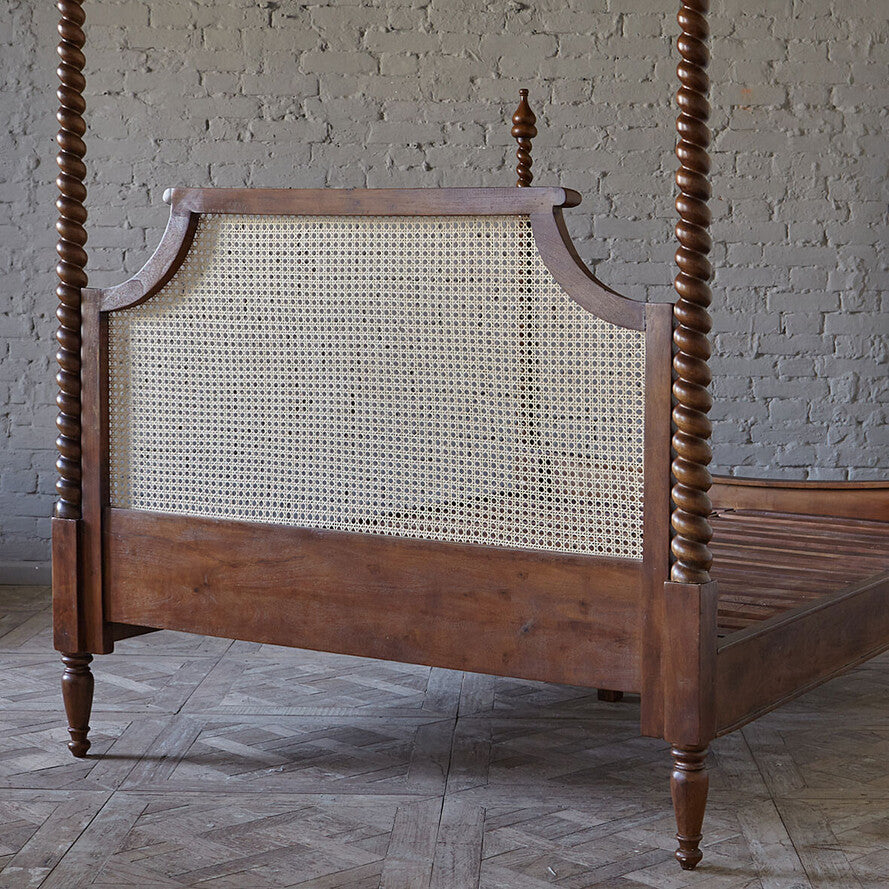 Wooden four-poster bed with cane backrest against a brick wall.