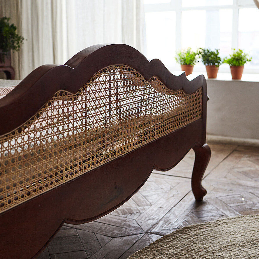 Wooden bed with wicker headboard in a room with plants and natural light