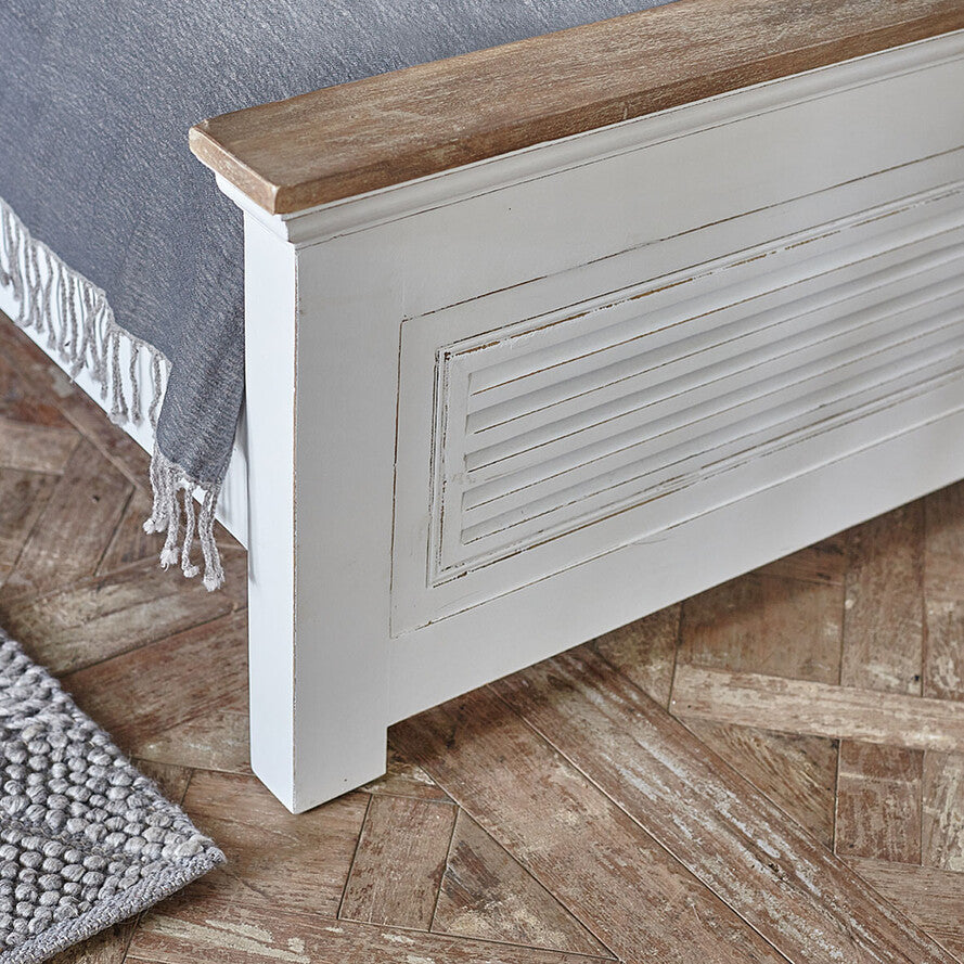 Close-up of a wooden bed with a white baseboard on a wooden floor.