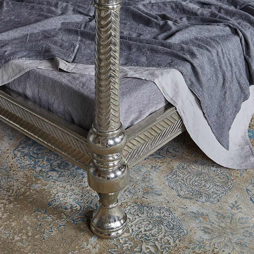 Silver bed frame with intricate design on a textured rug