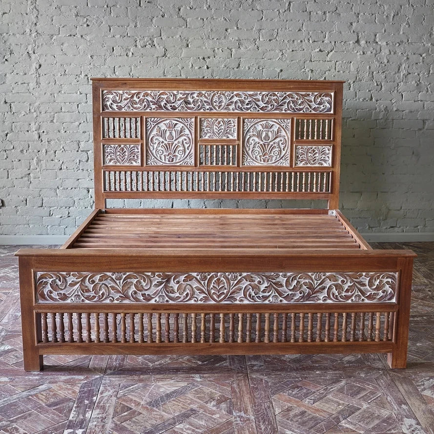 Wooden bed with intricate carvings against a brick wall.