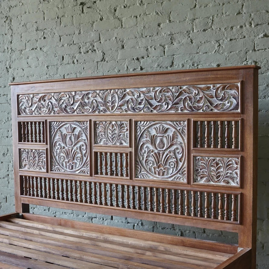 Wooden headboard with intricate carvings against a brick wall.