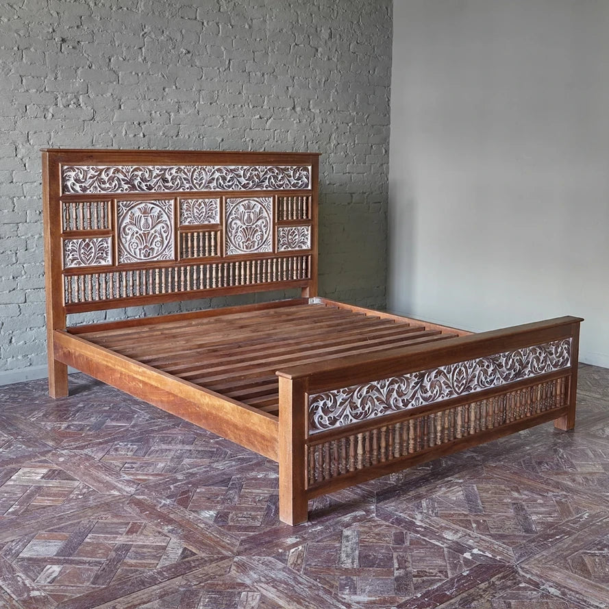 Wooden bed with intricate carvings against a gray brick wall.