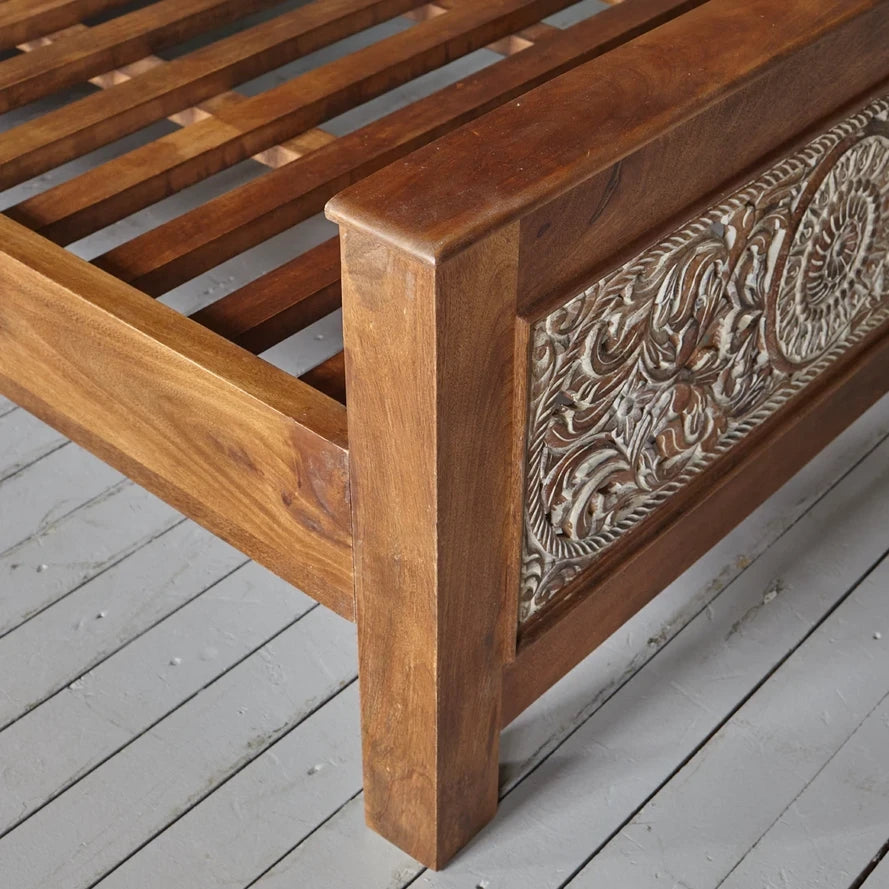 Wooden bed frame with intricate carvings on a wooden floor