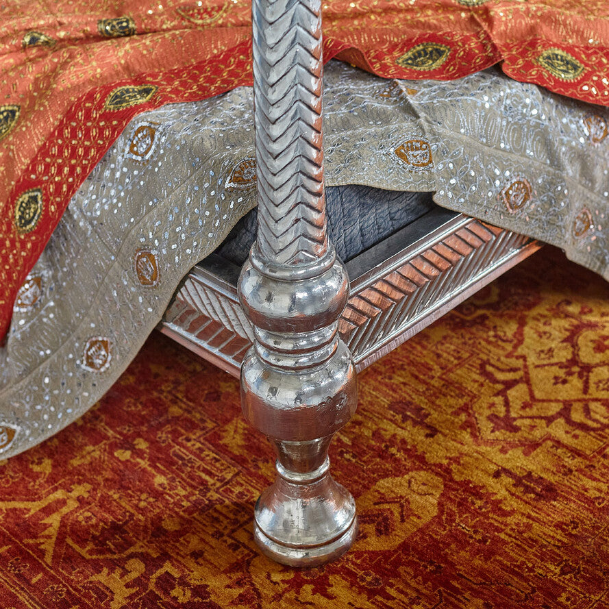 Decorative chair with red and gold fabric and a silver metal leg on a patterned rug.